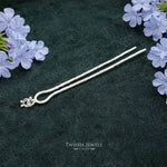 Silver hairpin on a dark green surface with purple flowers