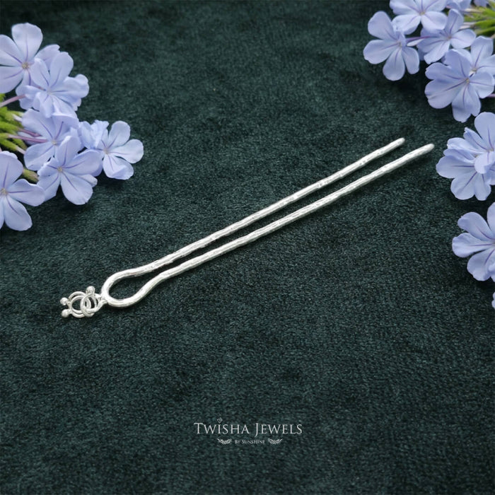 Silver hairpin on a dark green surface with purple flowers